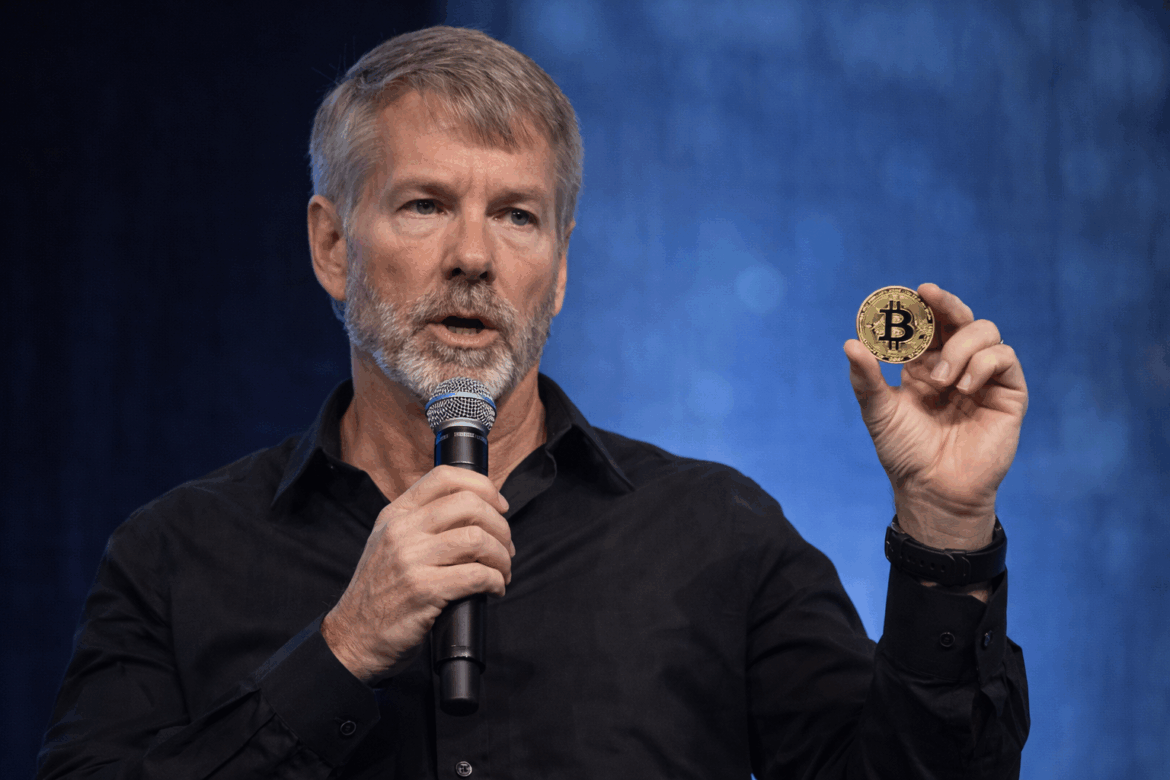 Michael Saylor speaking on stage while holding a physical Bitcoin coin